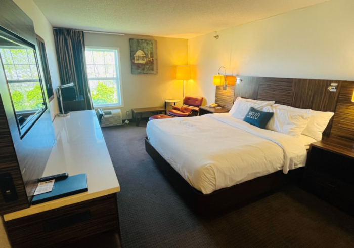 Hotel room with a large bed, desk, windows, and warm lamp light