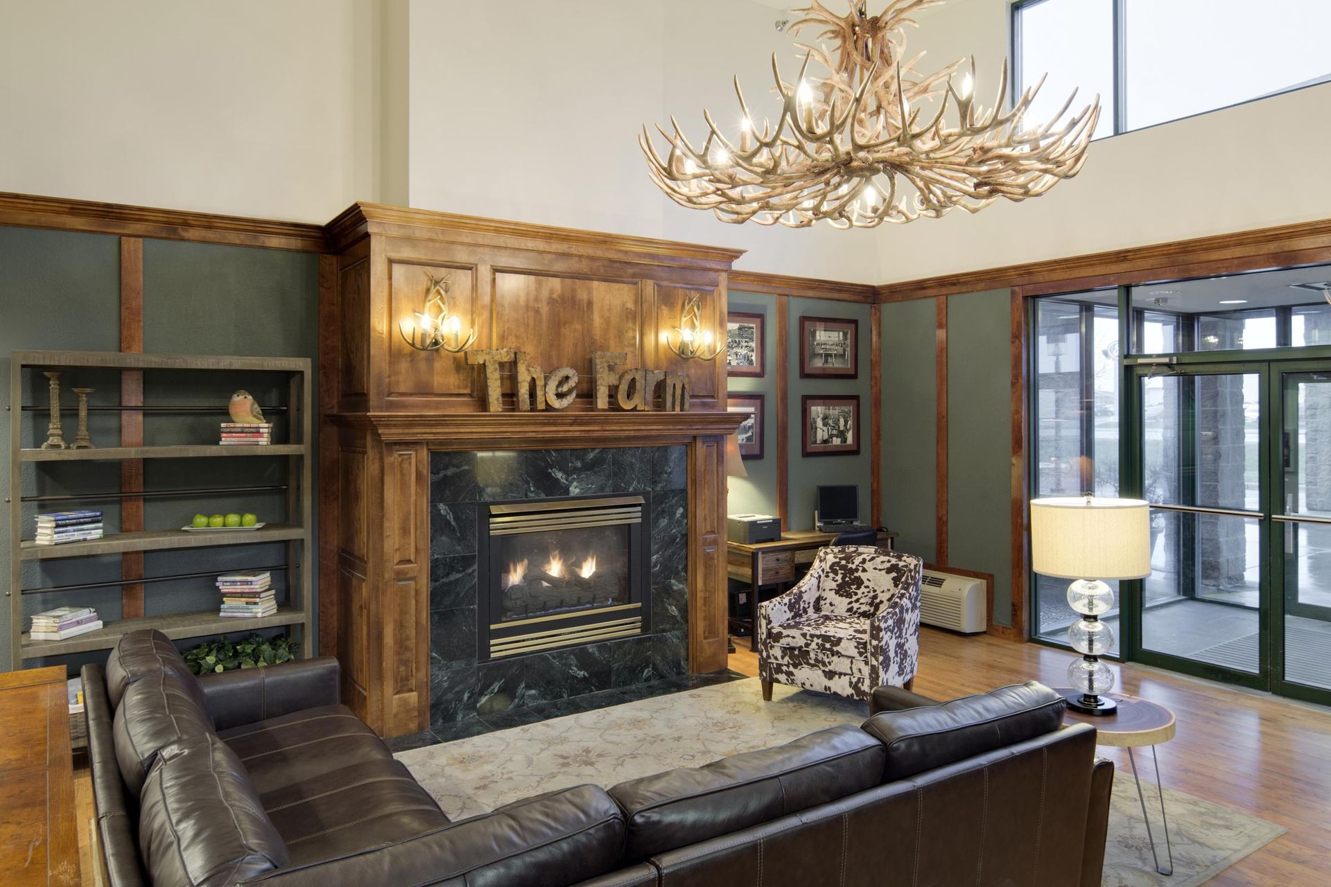 Elegant living room with wood-paneled fireplace, chandelier, leather sofa, and large windows