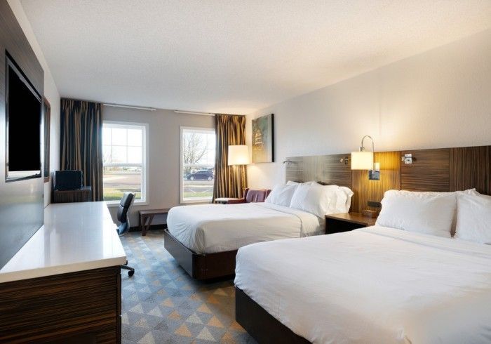 Modern hotel room with two beds, desk, chairs, and large window with city view