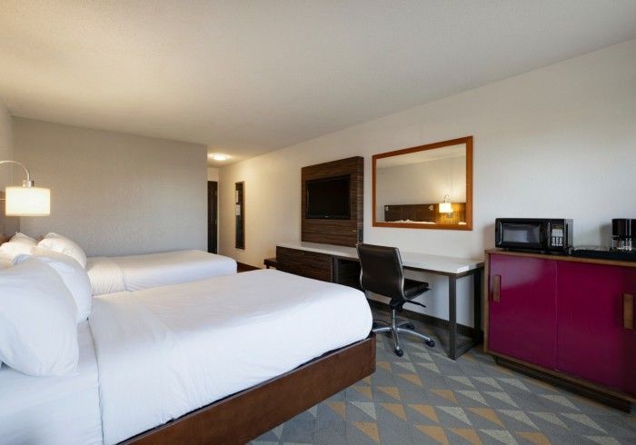 Hotel room with two beds, desk, mirror, and magenta cabinet in a modern interior
