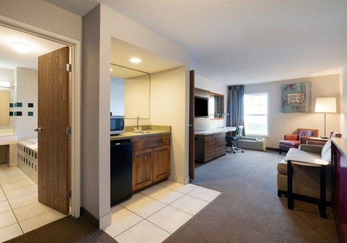 Hotel room with kitchenette, TV, bed, desk, and bright window seating area
