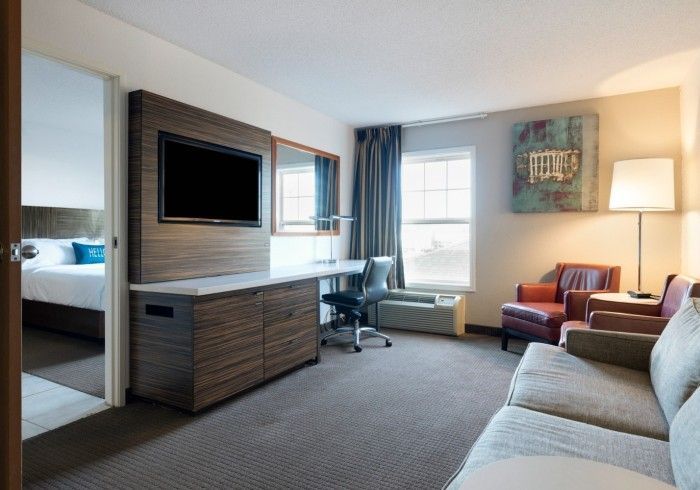 Modern hotel room with two beds, desk, TV, armchair, floor lamp, and window with curtains