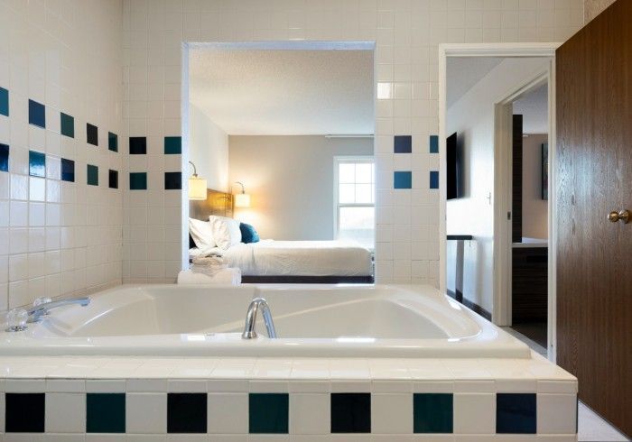 Bathroom with tiled tub and mirror reflecting a bedroom beyond the doorway