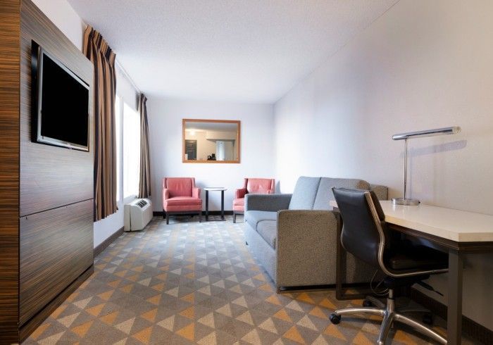 Modern hotel room with desk, chair, sofa, and two red armchairs by a window