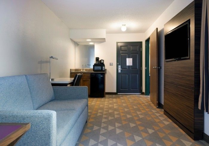 Modern hotel room with blue sofa, desk area, wall-mounted TV, and blue door.
