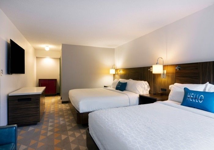 Hotel room with two white beds, wall-mounted TV, lamps, and a patterned carpet