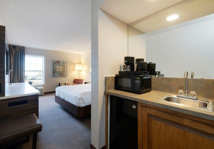 Hotel suite with bed and kitchenette, including a sink, coffee maker, and windowed sitting area