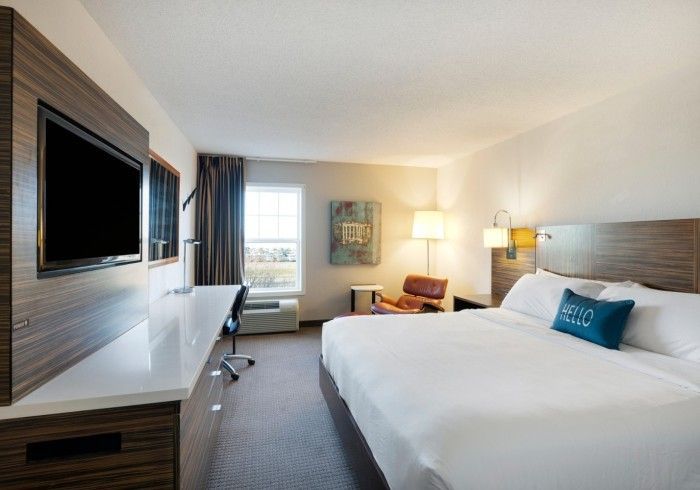 Modern hotel room with king bed, wall-mounted TV, desk, window, and lamp lighting