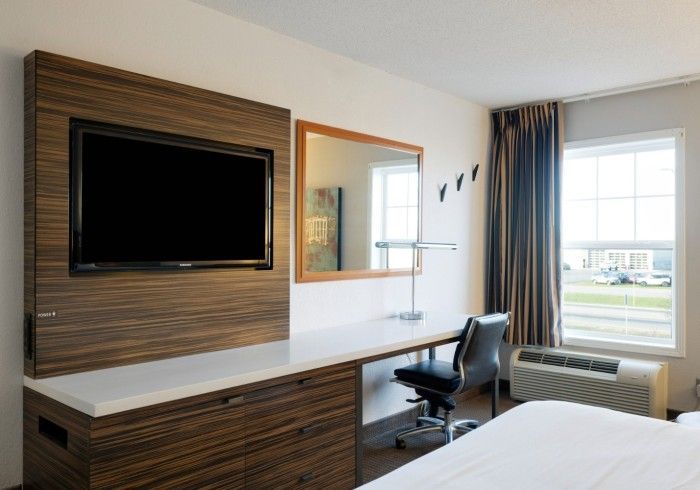 Modern hotel room with wall-mounted TV, desk, chair, bed, and window view