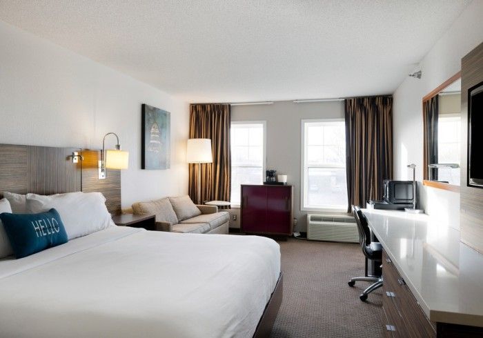 Modern hotel room with a bed, sofa, desk, large windows, and a wall mirror