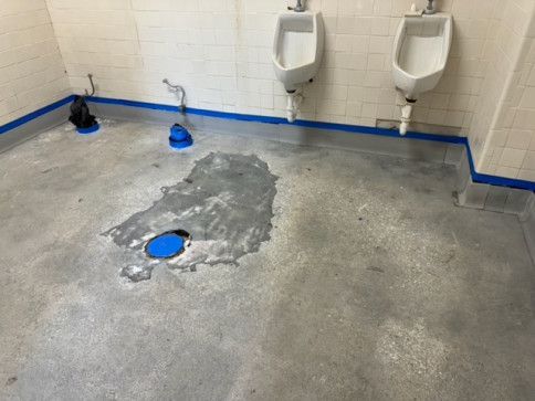 A bathroom with two urinals and a blue flange on the floor.