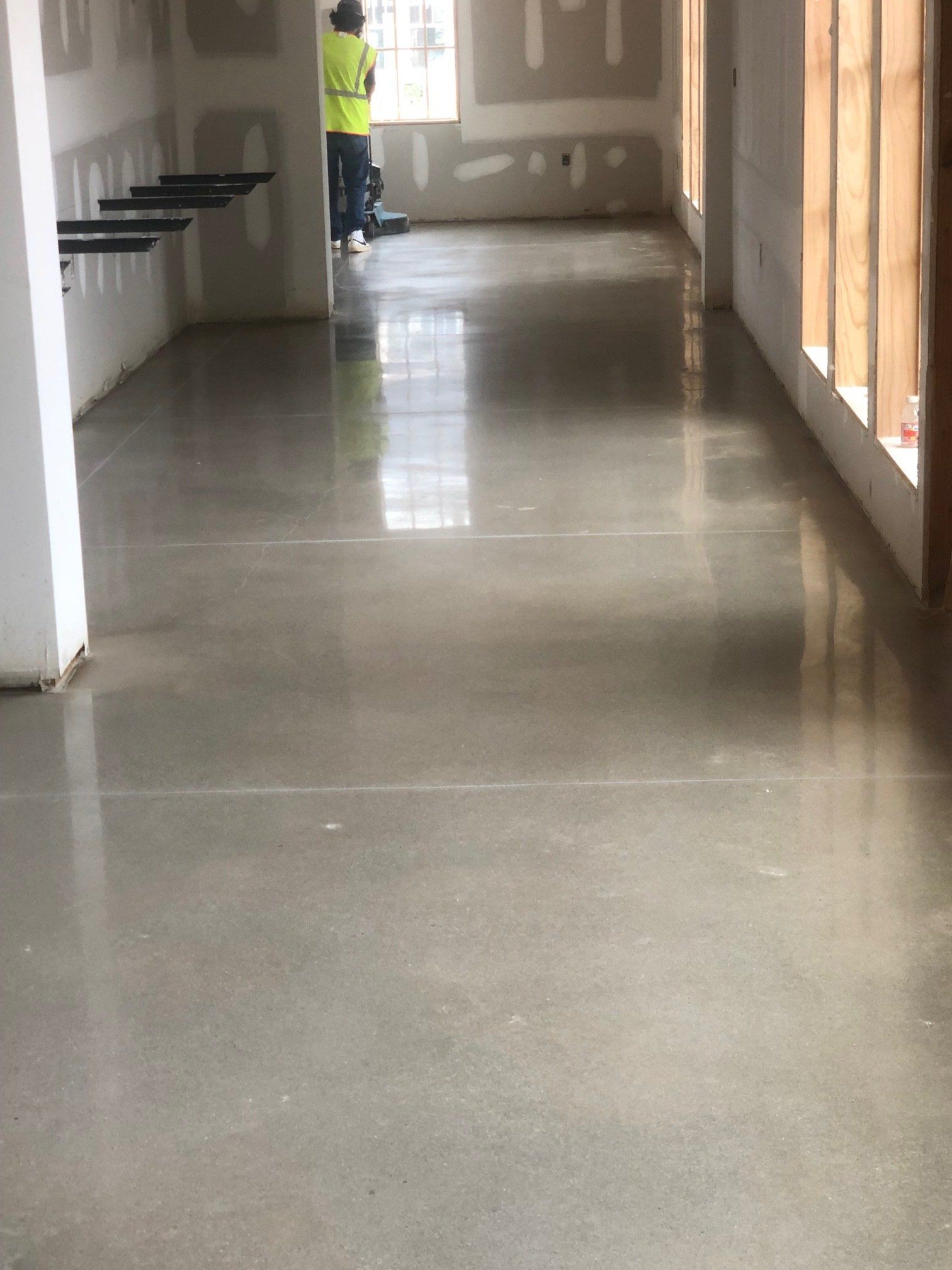 A man in a yellow vest is standing in a hallway with a shiny concrete floor.