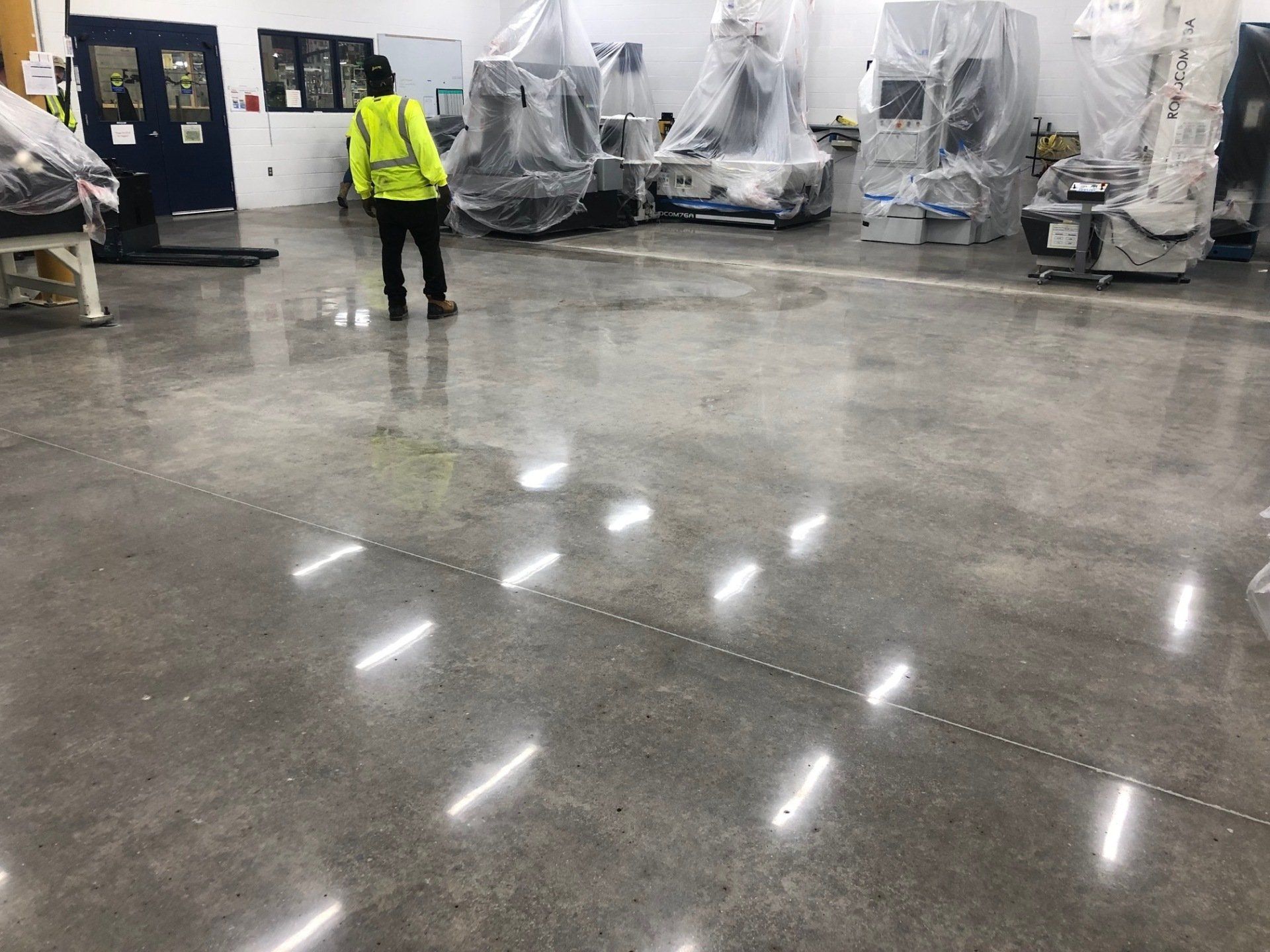 A man in a yellow vest is standing in a large room with lots of machines.