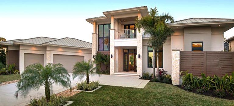 Modern two-story house with a landscaped front yard, palm trees, and a driveway at sunset