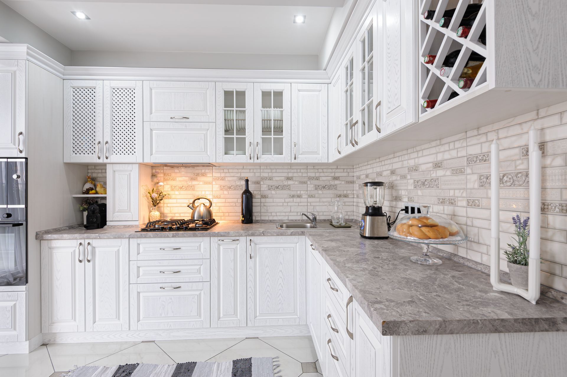 Bright white kitchen with gray countertops, tiled backsplash, and built-in cabinetry
