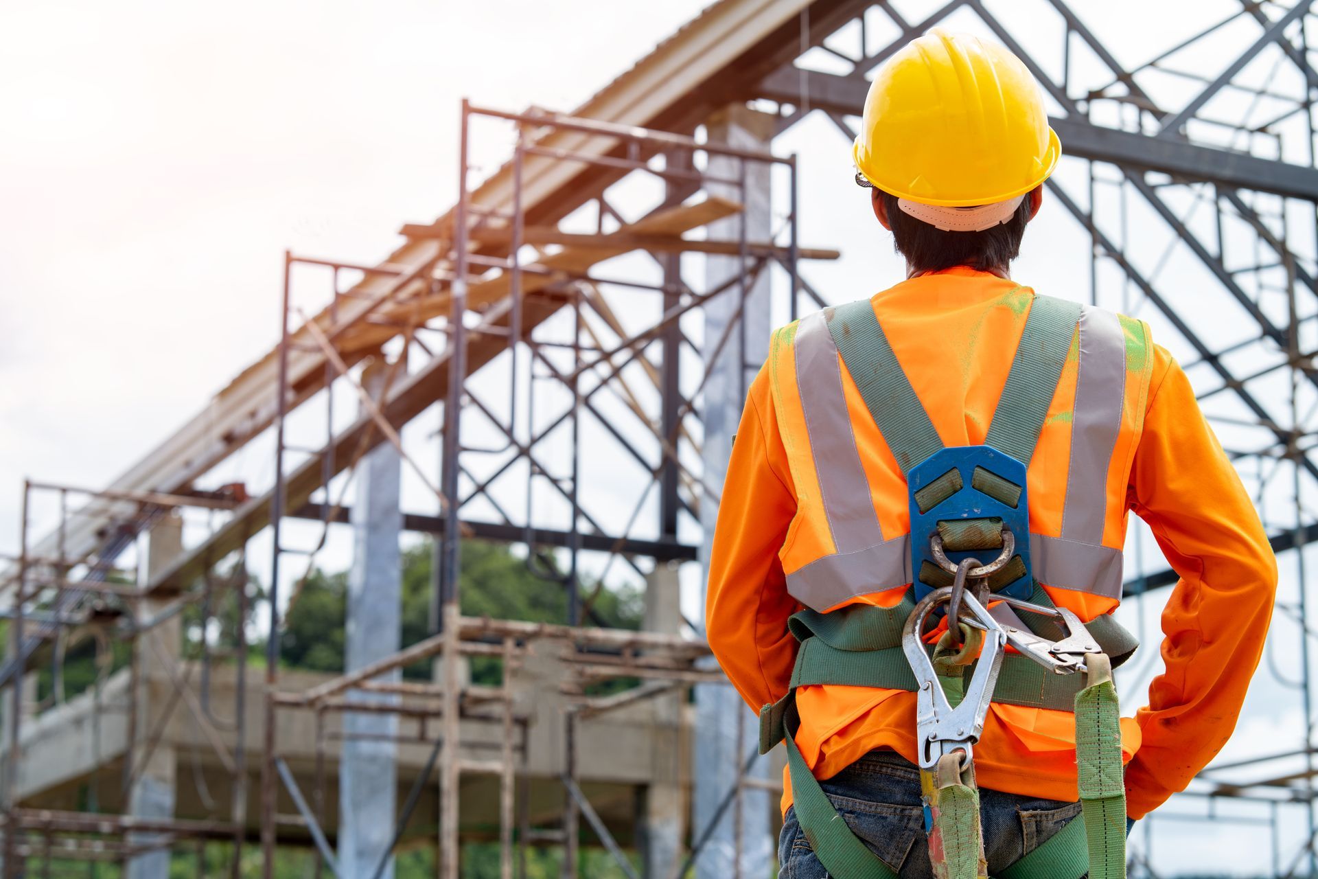 Construction worker in orange safety gear and hard hat overlooking a steel framework site