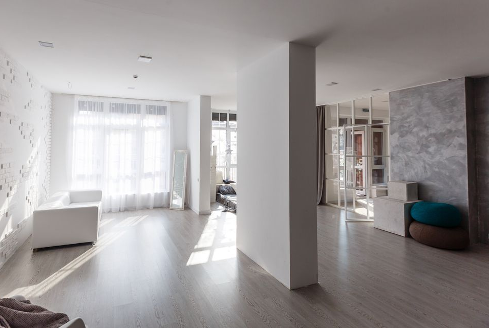 Bright minimalist living room with white walls, light wood floors, large windows, and a teal chair.