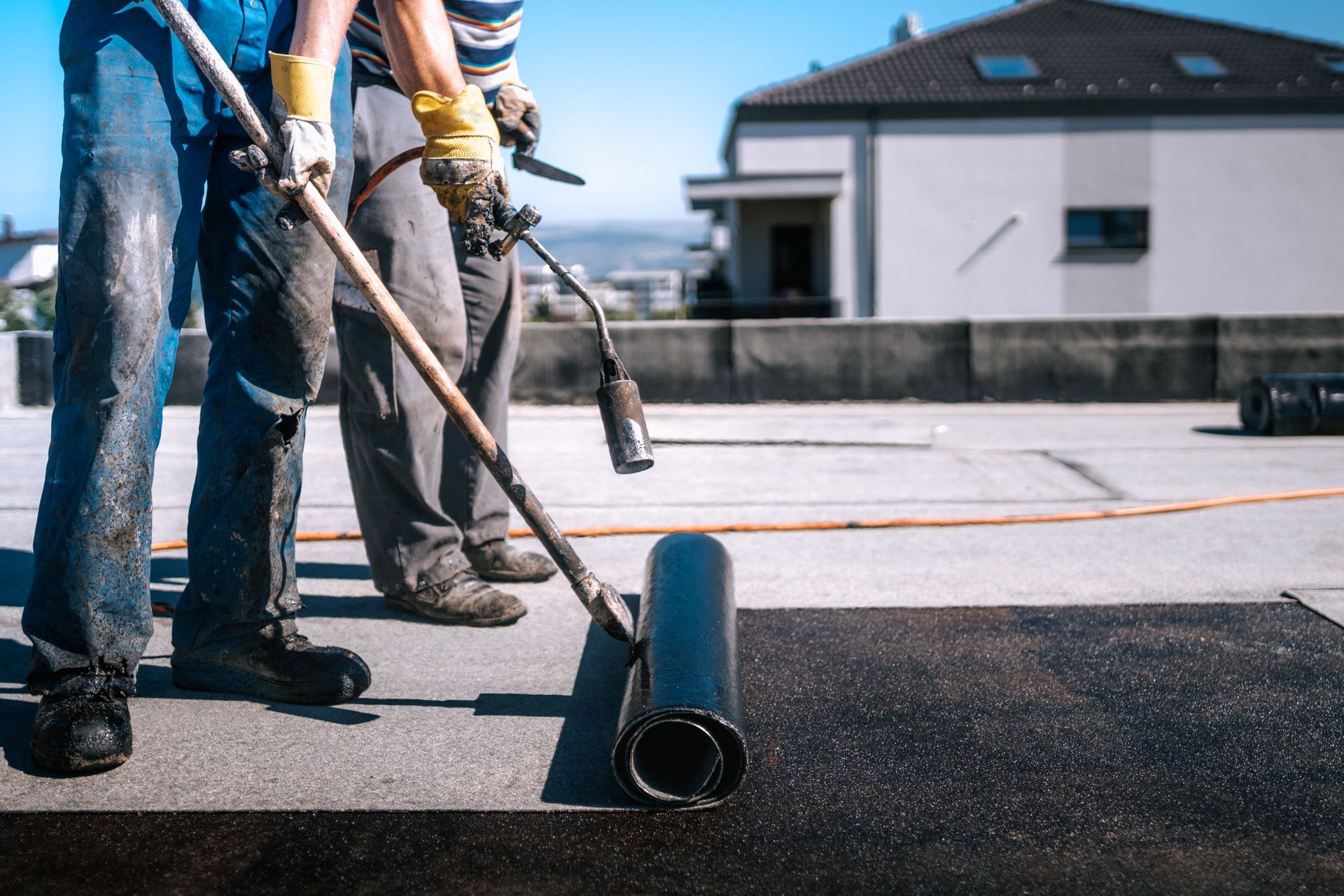 Workers using rollers to apply black roofing material on a flat rooftop