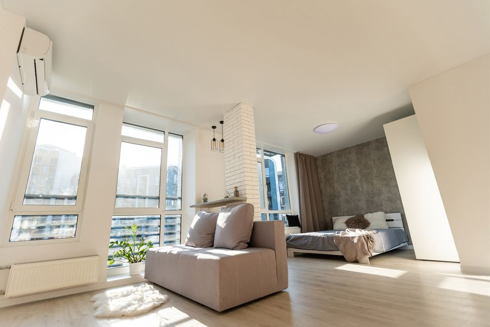 Bright modern bedroom and living area with sofa, bed, large windows, and balcony view