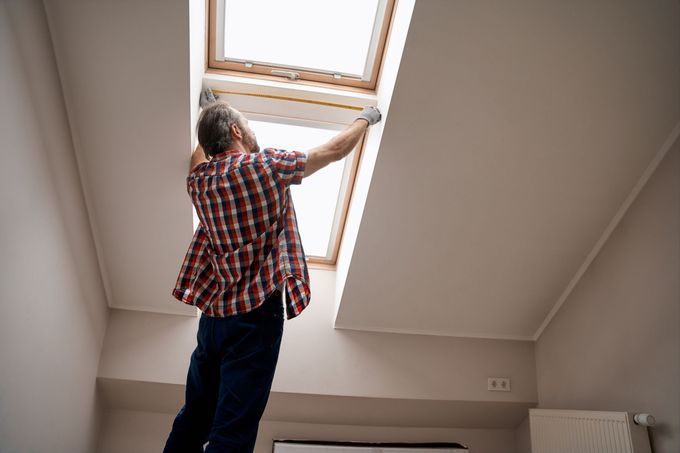 Person opening a skylight window indoors in a room with slanted walls.