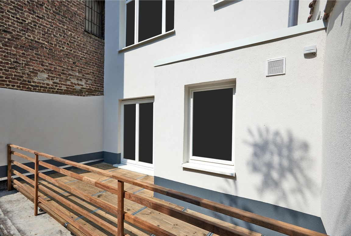 White building exterior with windows and a wooden railing along a sunny walkway