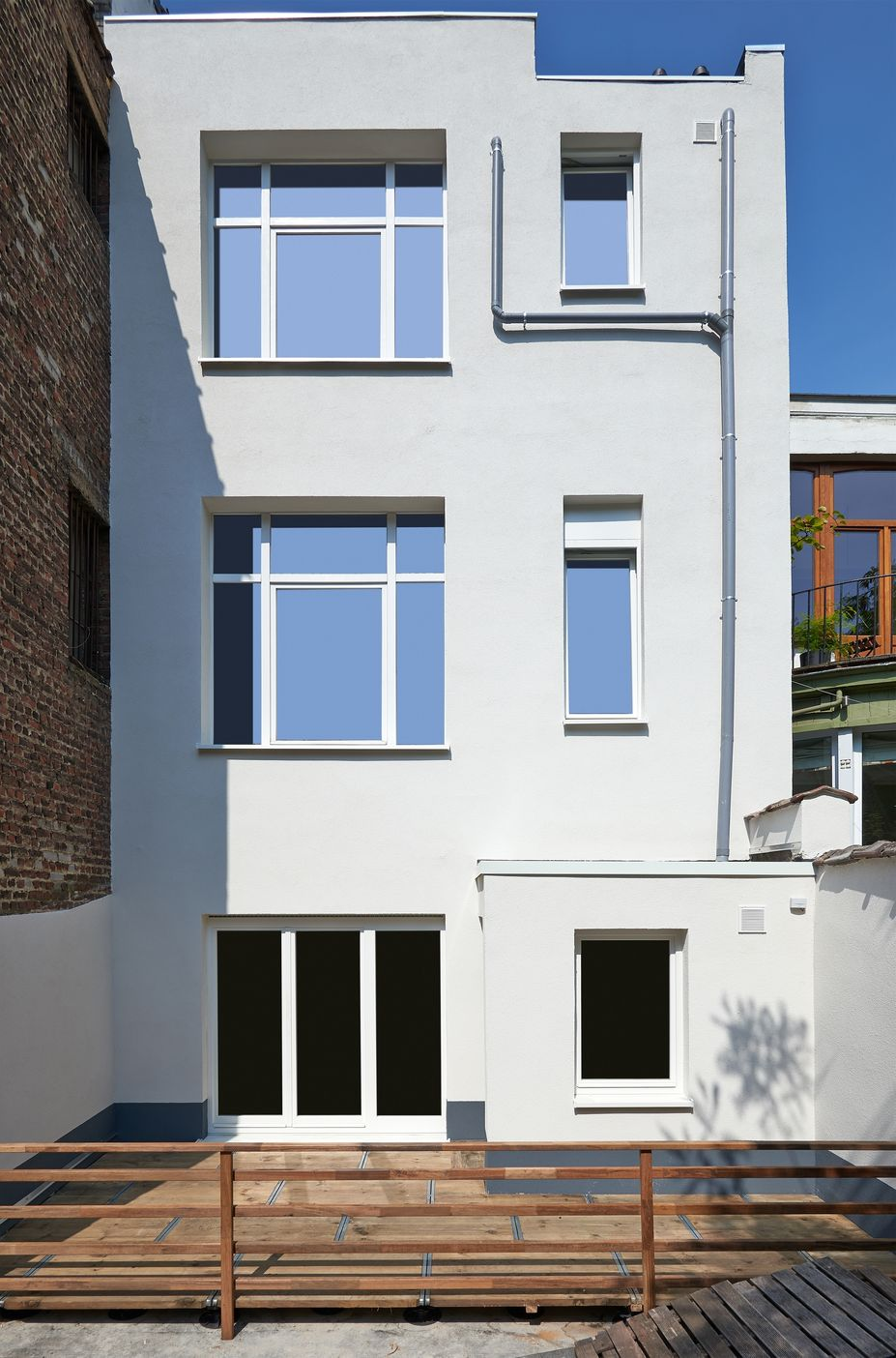 White three-story townhouse facade with large windows and ground-level doors, viewed from the street