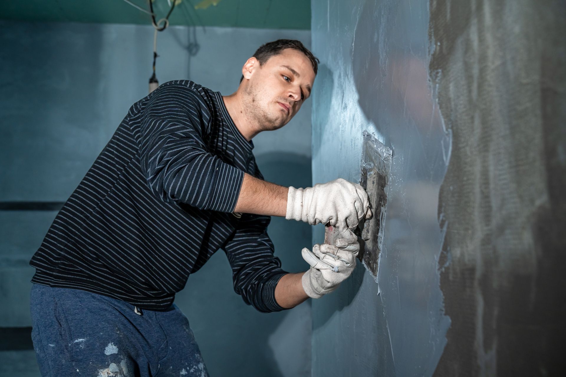 Worker smoothing gray plaster on a wall with a trowel in an unfinished room