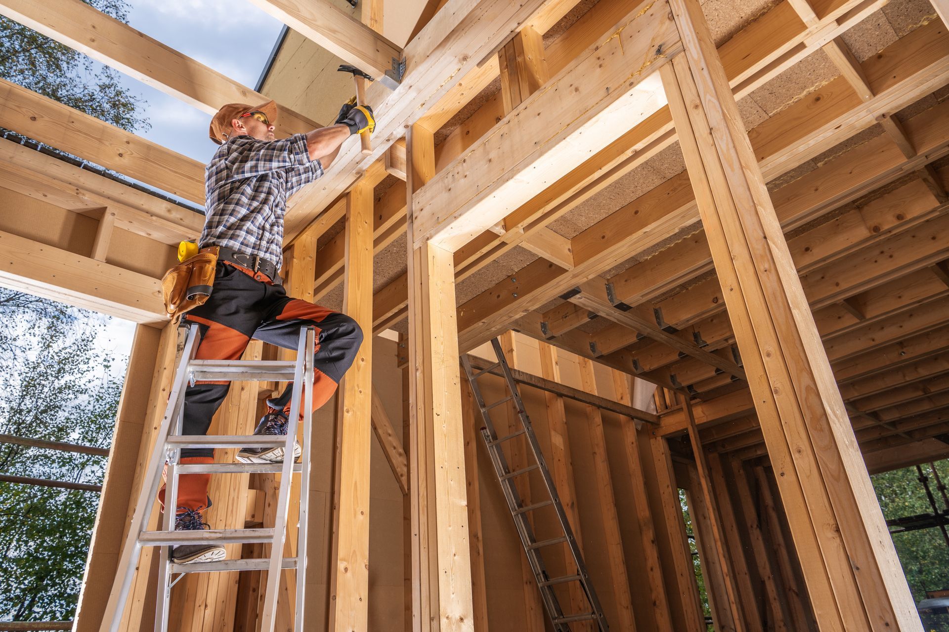 Worker on a ladder installing wooden framing in a house under construction.