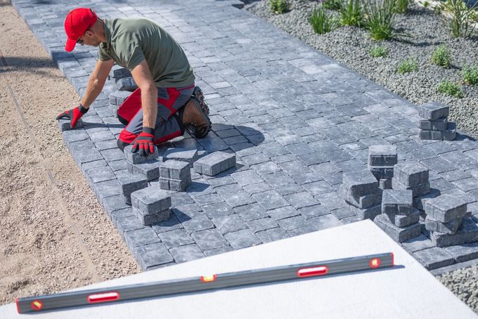 Worker laying gray pavers with a level on a gravel path