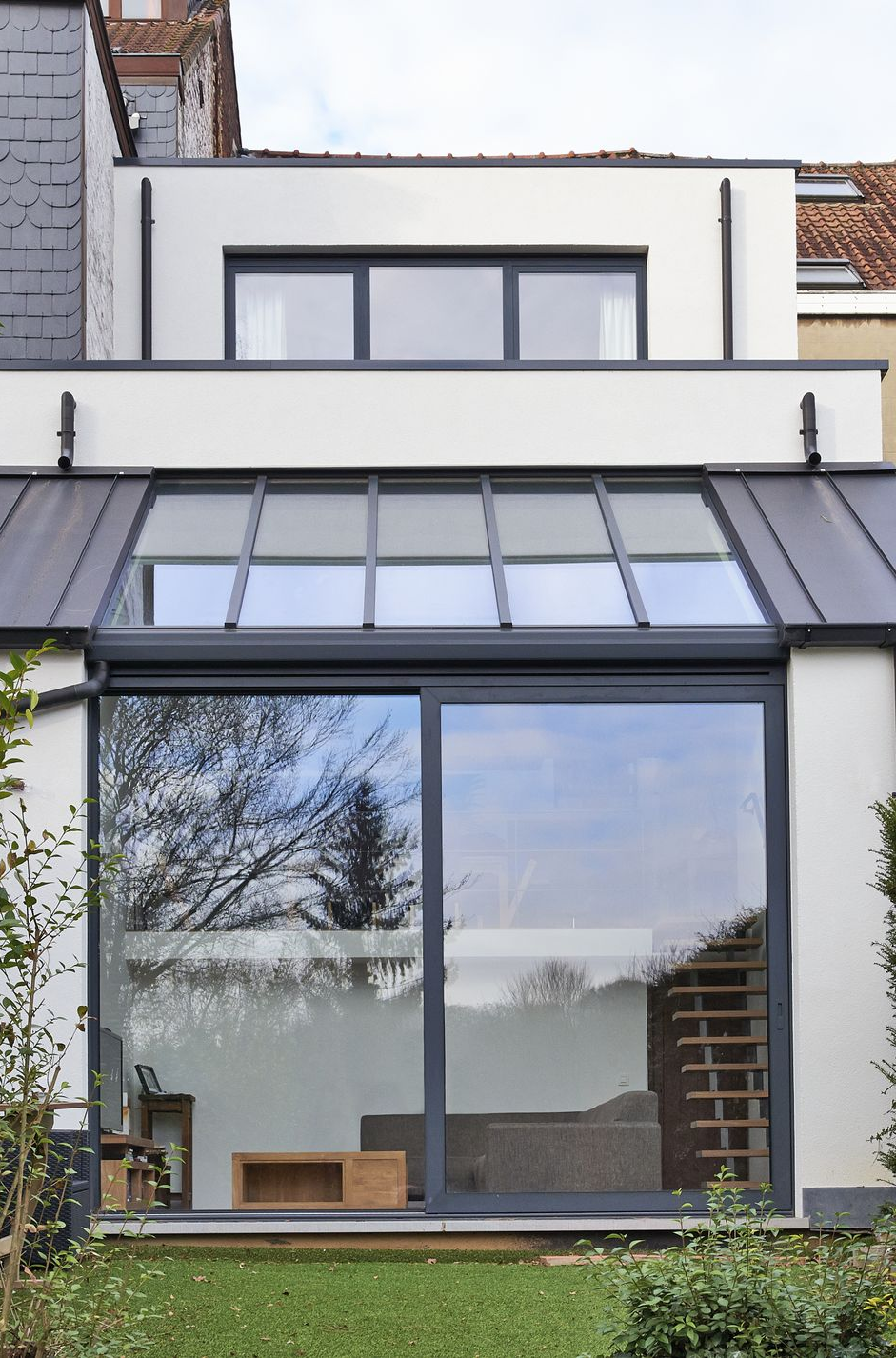 Modern two-story house facade with large glass windows and a dark metal roof