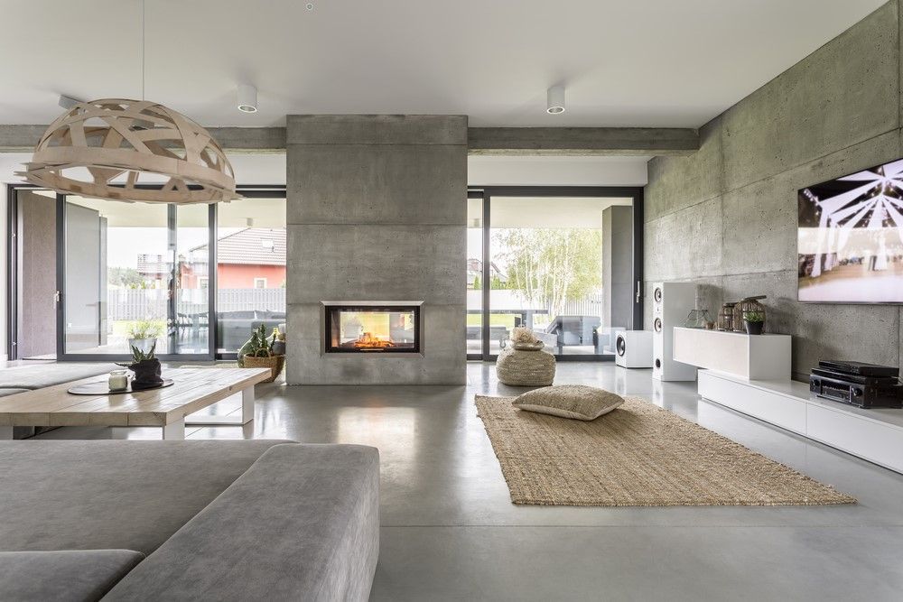 Modern living room with concrete fireplace, large windows, gray sectional, and white TV console