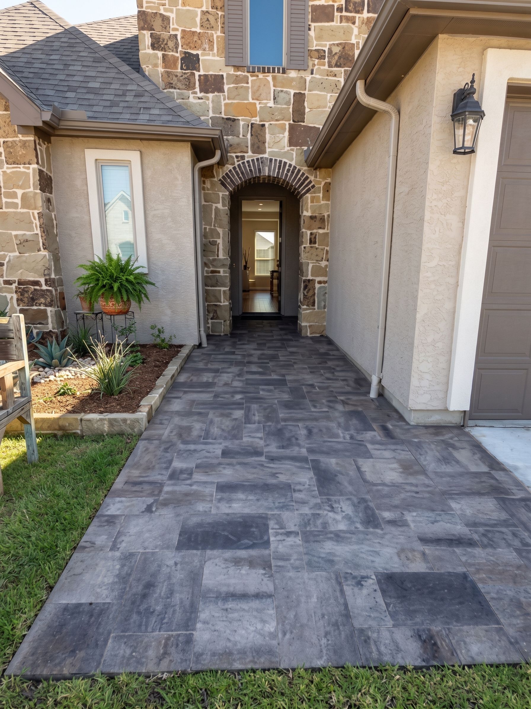 Stone walkway leading to a front entry with an arched doorway and beige stucco house exterior
