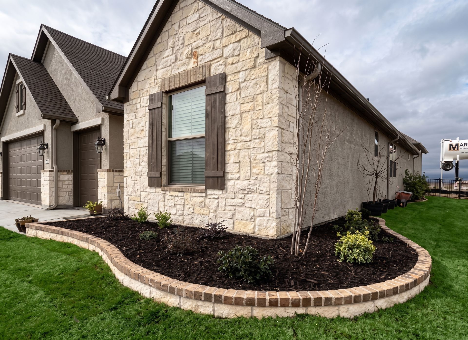 Stone house exterior with arched windows, manicured lawn, and curved brick garden bed under a cloudy sky