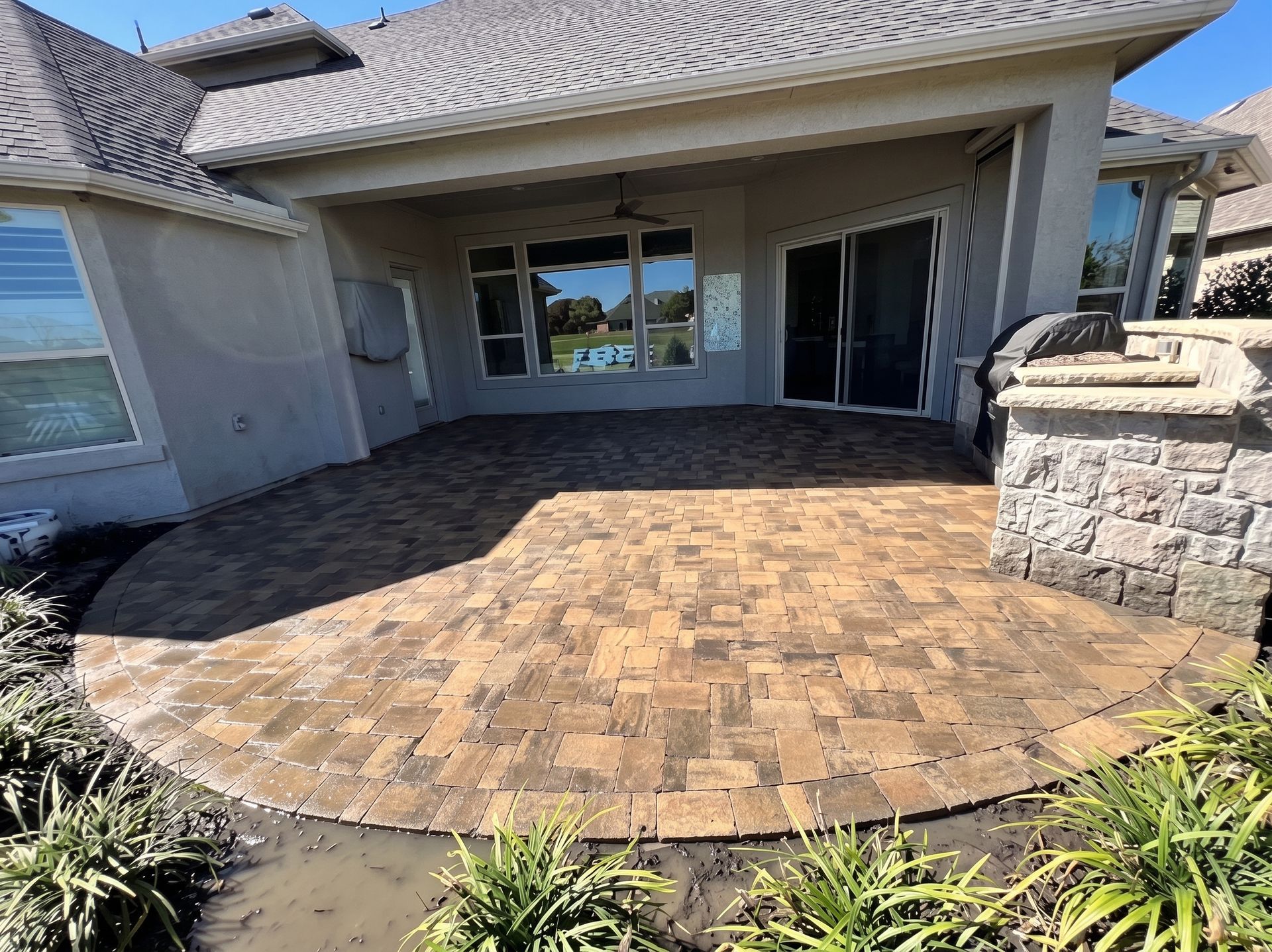 Brick paver patio in front of a house with covered patio and stone planter walls
