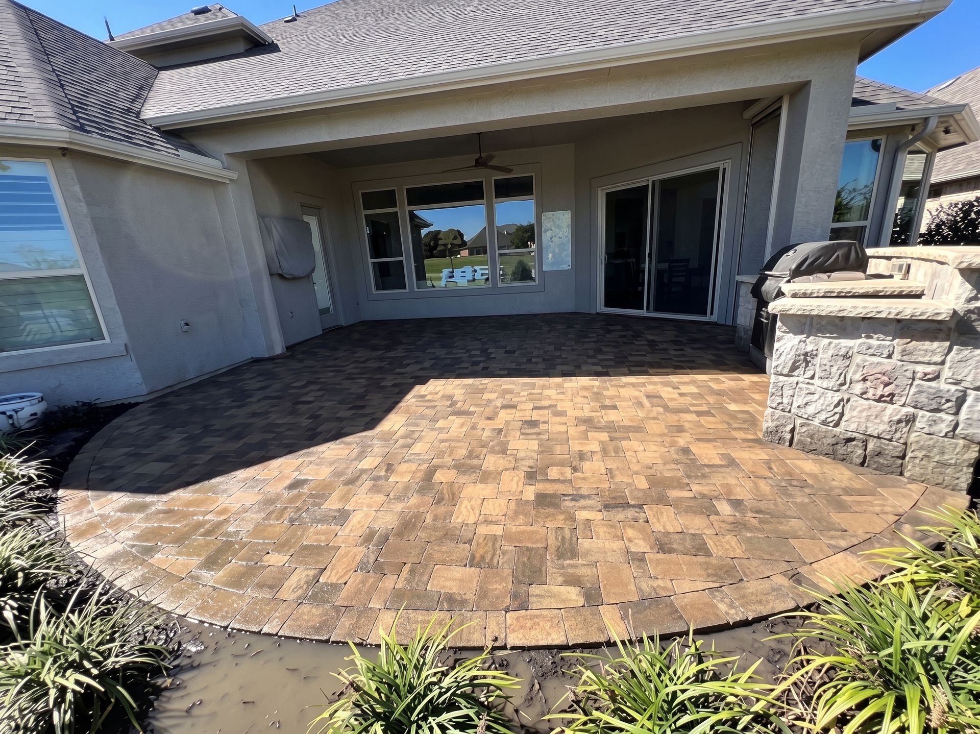 Covered brick patio with sliding glass doors and stone planter wall in front of a house