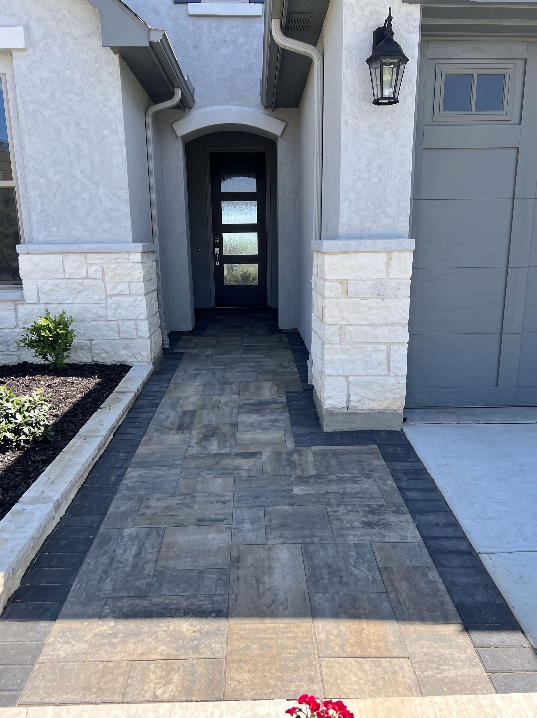 Front walkway to a house entrance with gray paver path, white stone columns, and a gray garage door