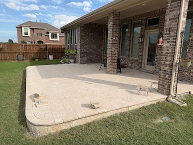 Backyard patio with beige stone pavers and wooden fence in Denton TX