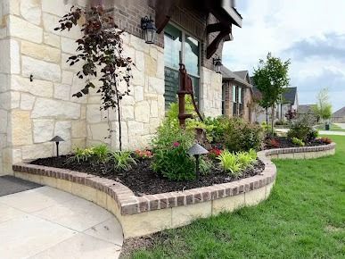 Front yard stone planter with shrubs and flowers beside house and driveway in Denton TX