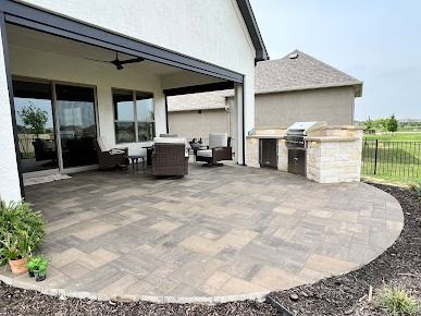 Covered patio with gray pavers and built-in stone fireplace beside home
