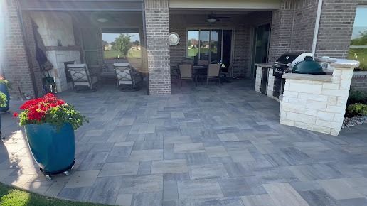 Covered patio with gray paver flooring and stone columns by Lonestar Customscapes