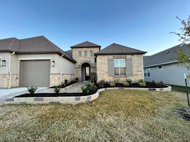 Single-story stone house with arched entry, two-car garage, and front lawn under a clear blue sky