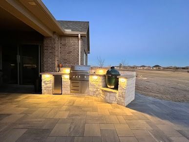 Outdoor patio with stone bar and warm lighting beside brick house at dusk
