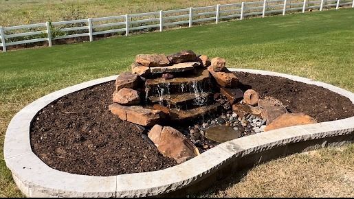 Small rock waterfall cascading into stone-bordered mulch bed in Denton TX