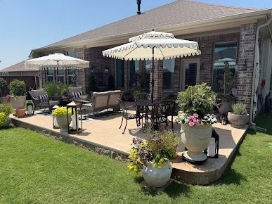 Patio with outdoor seating and white umbrellas beside brick house and lawn