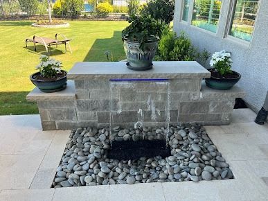 Stone water feature with water flowing into pebble basin on a patio