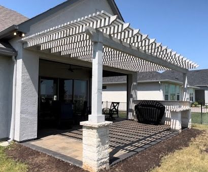 White pergola with stone pillars casting striped shadows on paver deck in Denton TX