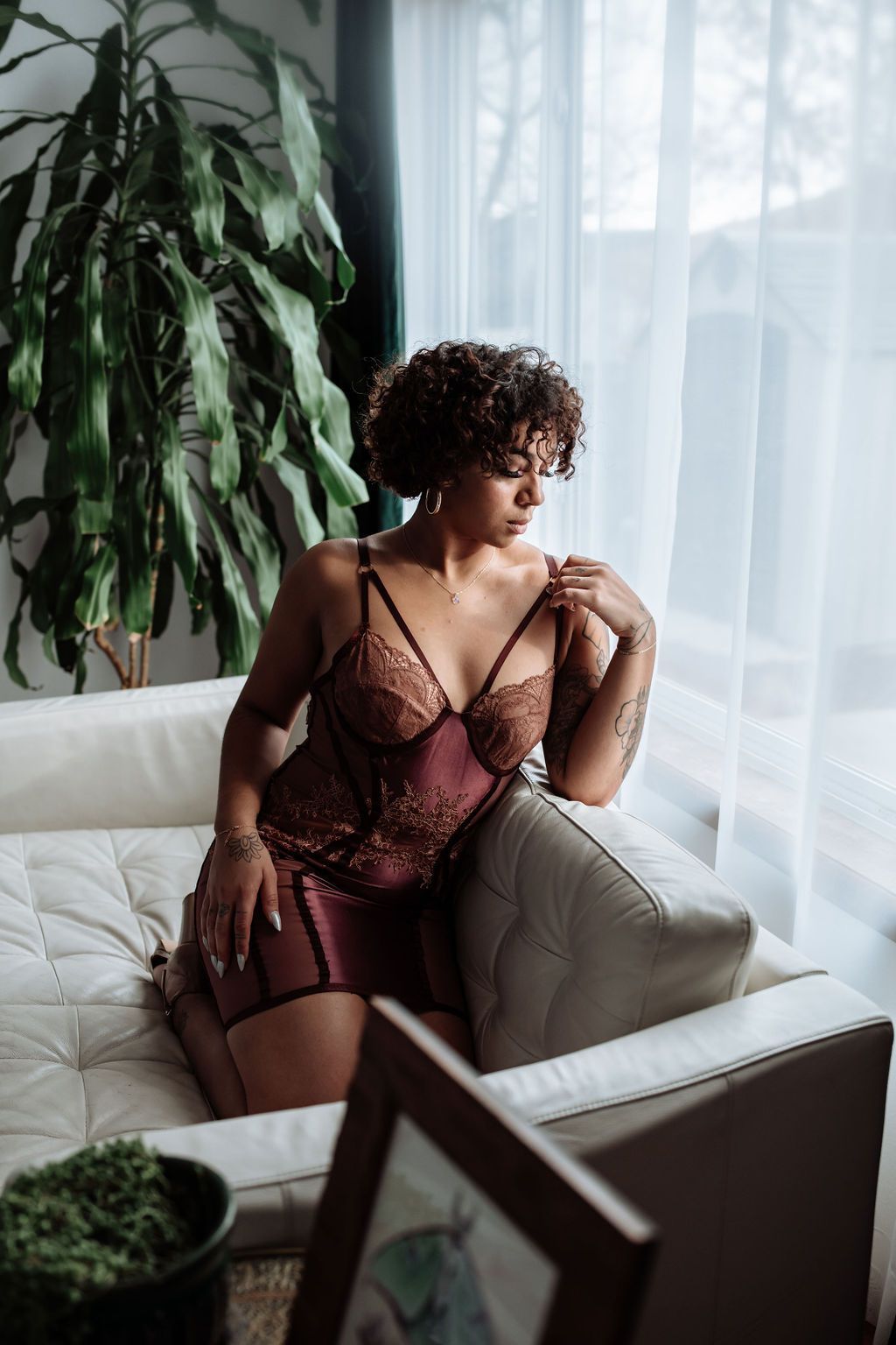 A woman in lingerie is sitting on a couch in front of a window.