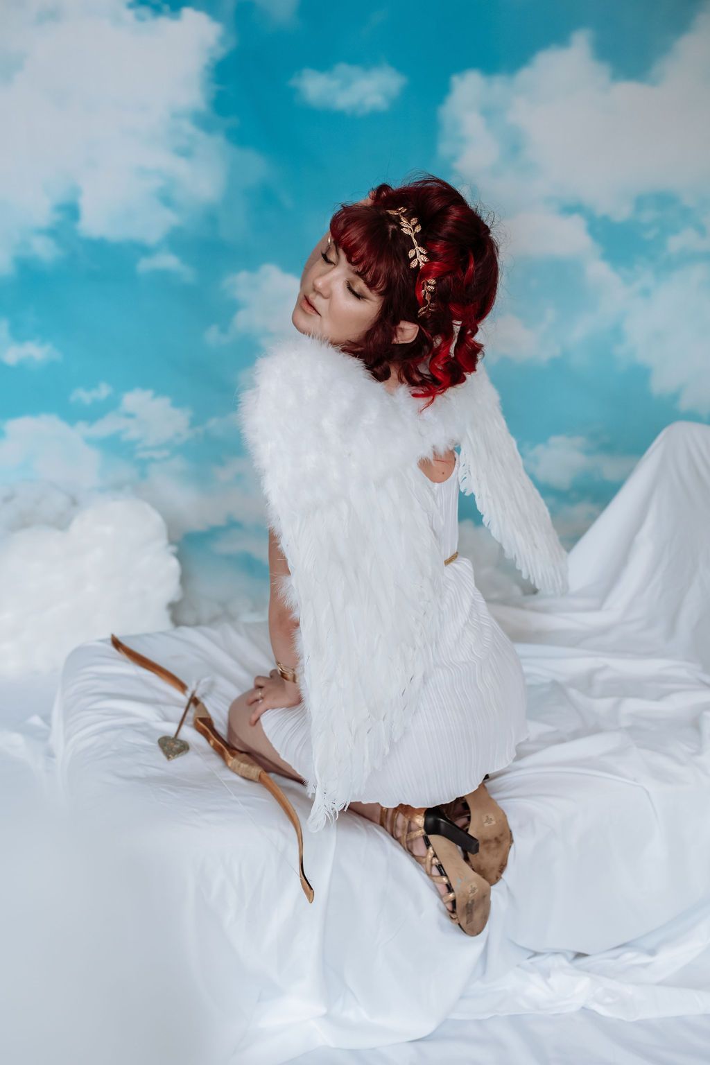 A woman dressed as a cupid is kneeling on a bed.