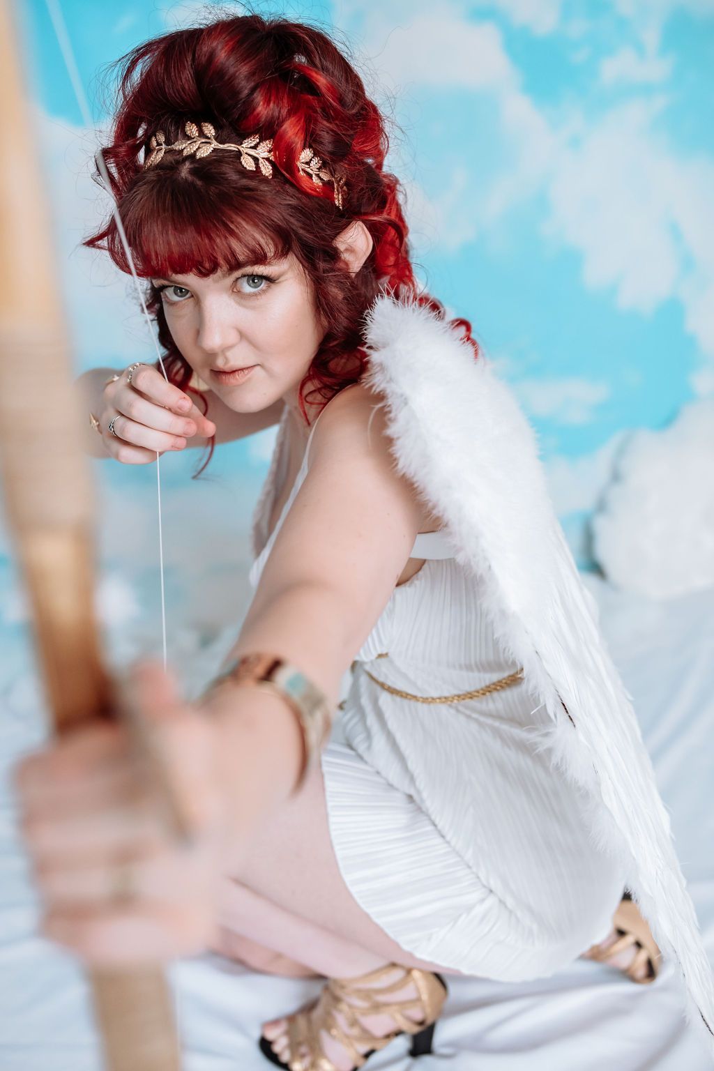 A woman facing the camera with wings on shooting an arrow towards the camera.