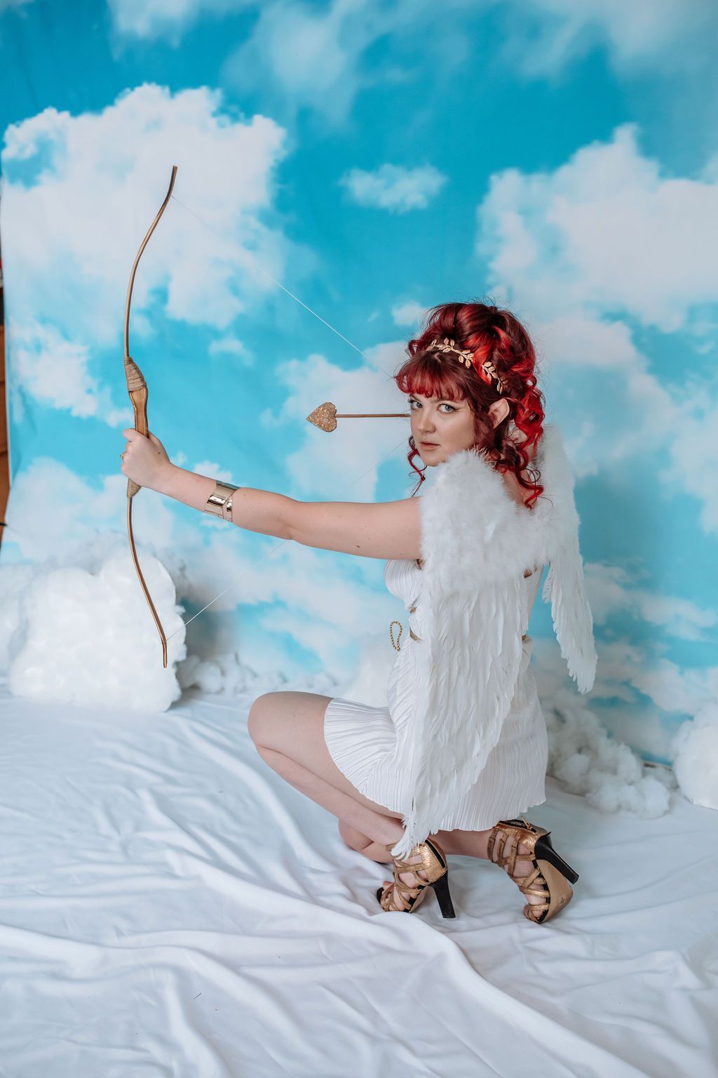 A woman dressed up as cupid with wings, holding a bow and arrow.